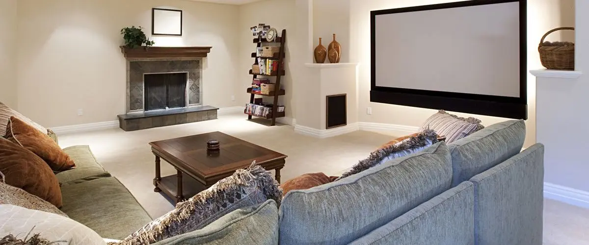 Modern remodeled basement with a cozy fireplace, large sectional sofa, and a built-in projector screen, ideal for family movie nights and relaxation.