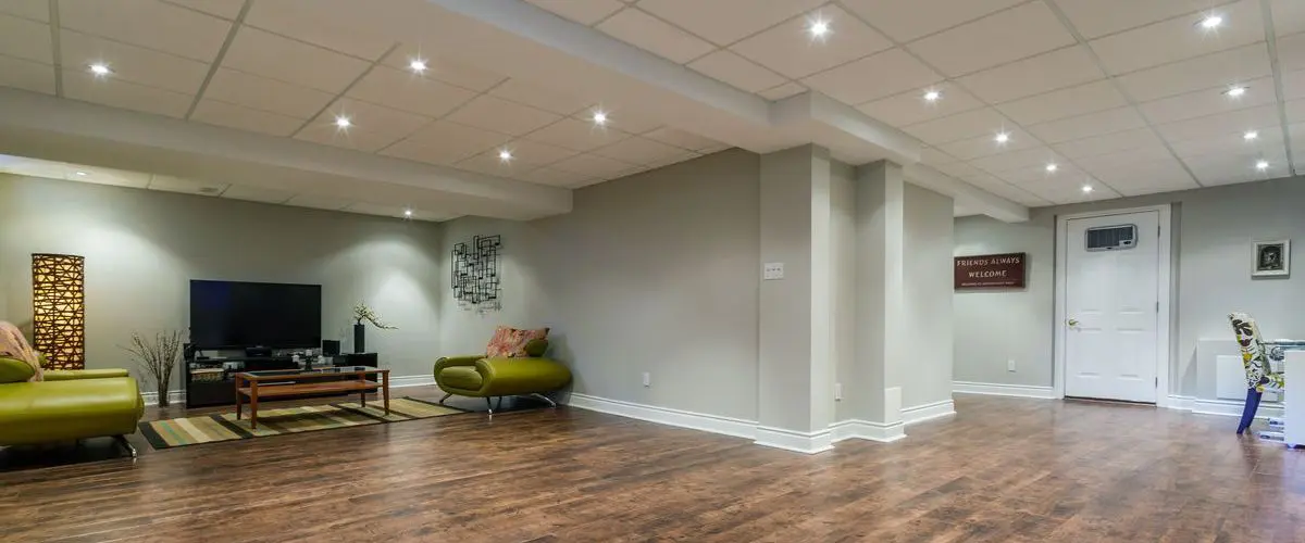 Spacious remodeled basement with modern lighting, wood flooring, and comfortable seating, perfect for a home entertainment area or lounging space.