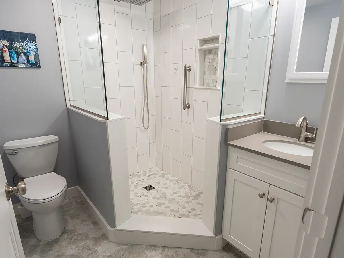 Small bathroom with glass-enclosed shower, white tiles, and gray vanity