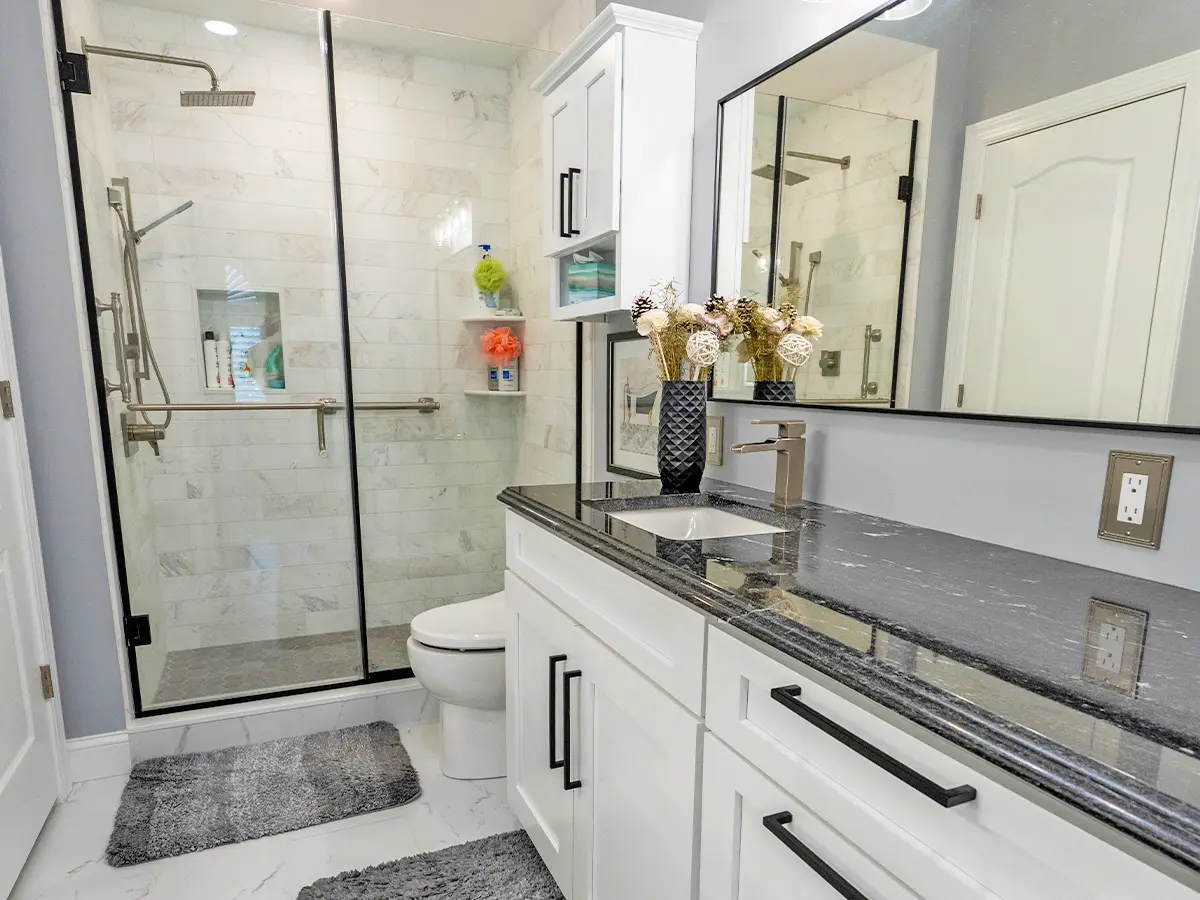 Modern bathroom with black granite countertop, white cabinets, and glass-enclosed shower