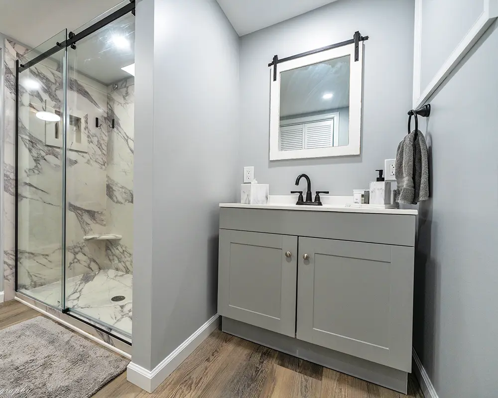 Modern bathroom with marble shower, gray vanity, and framed mirror.