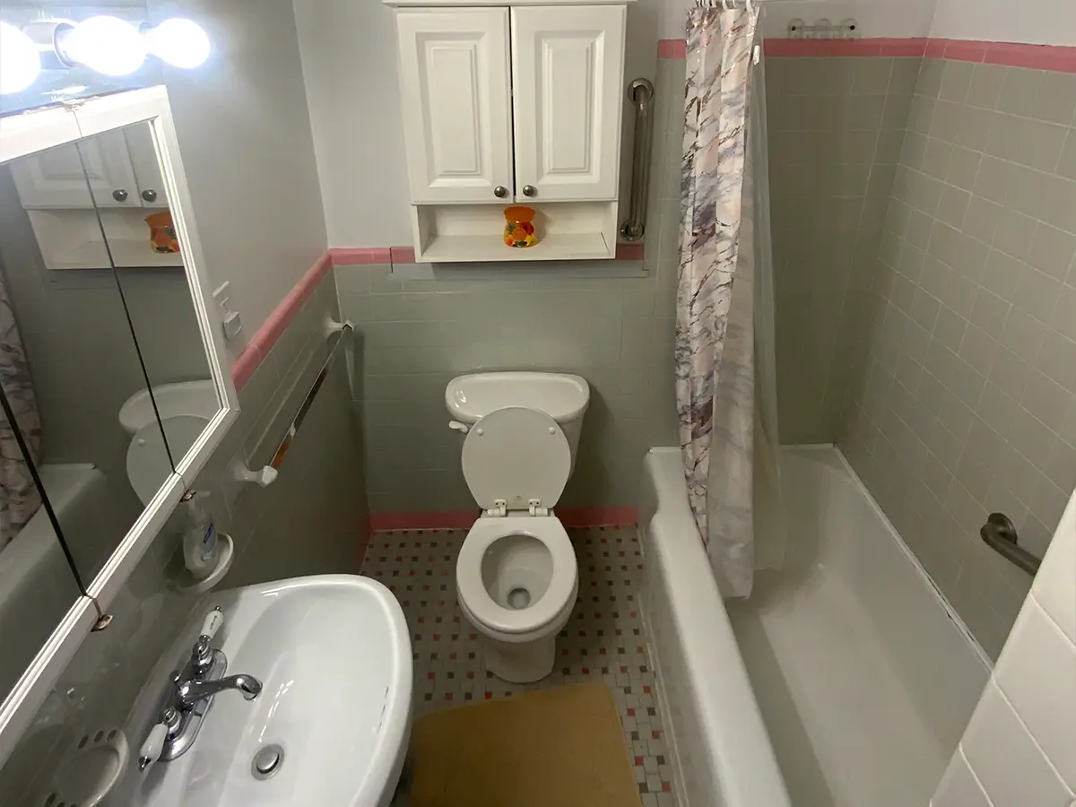 Outdated bathroom with pink and gray tiles, small vanity, and shower-tub combo