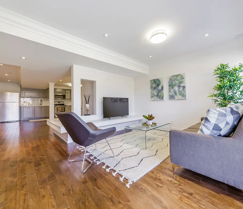 Modern living room with hardwood floors, glass coffee table, and open kitchen in the background